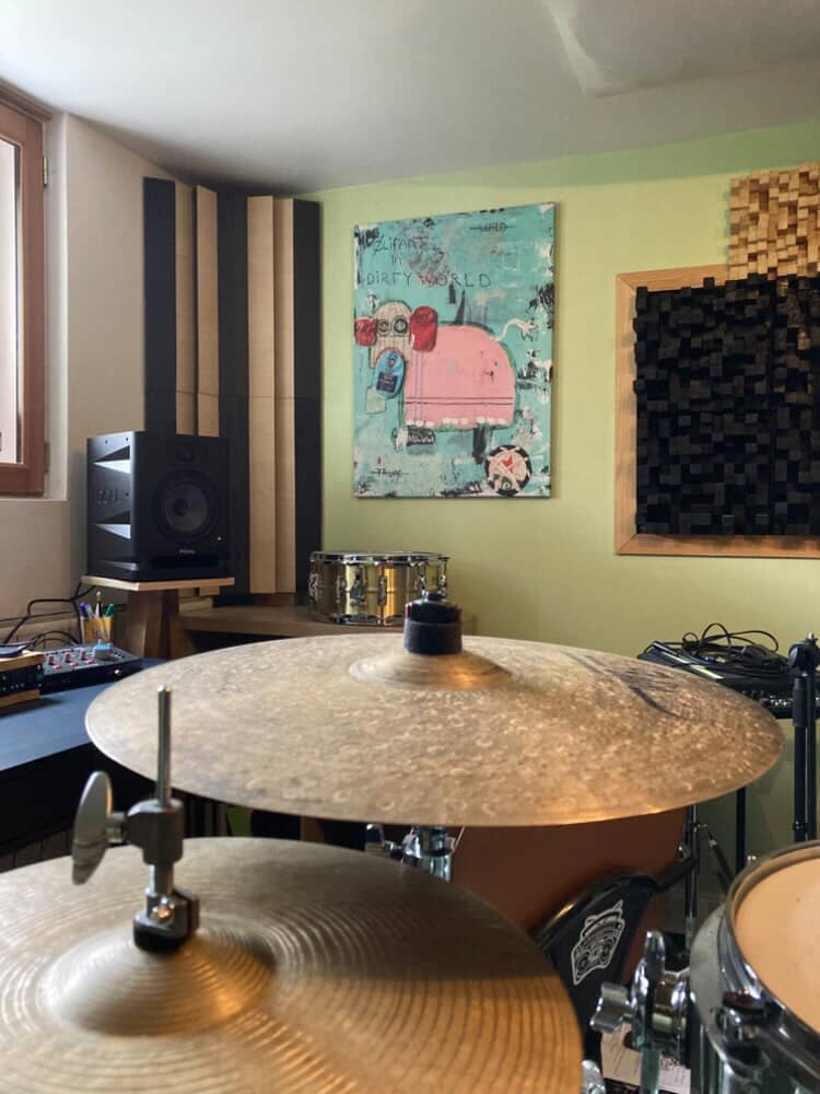 Drums set up in a room with soundproofing panels and artwork on the wall.