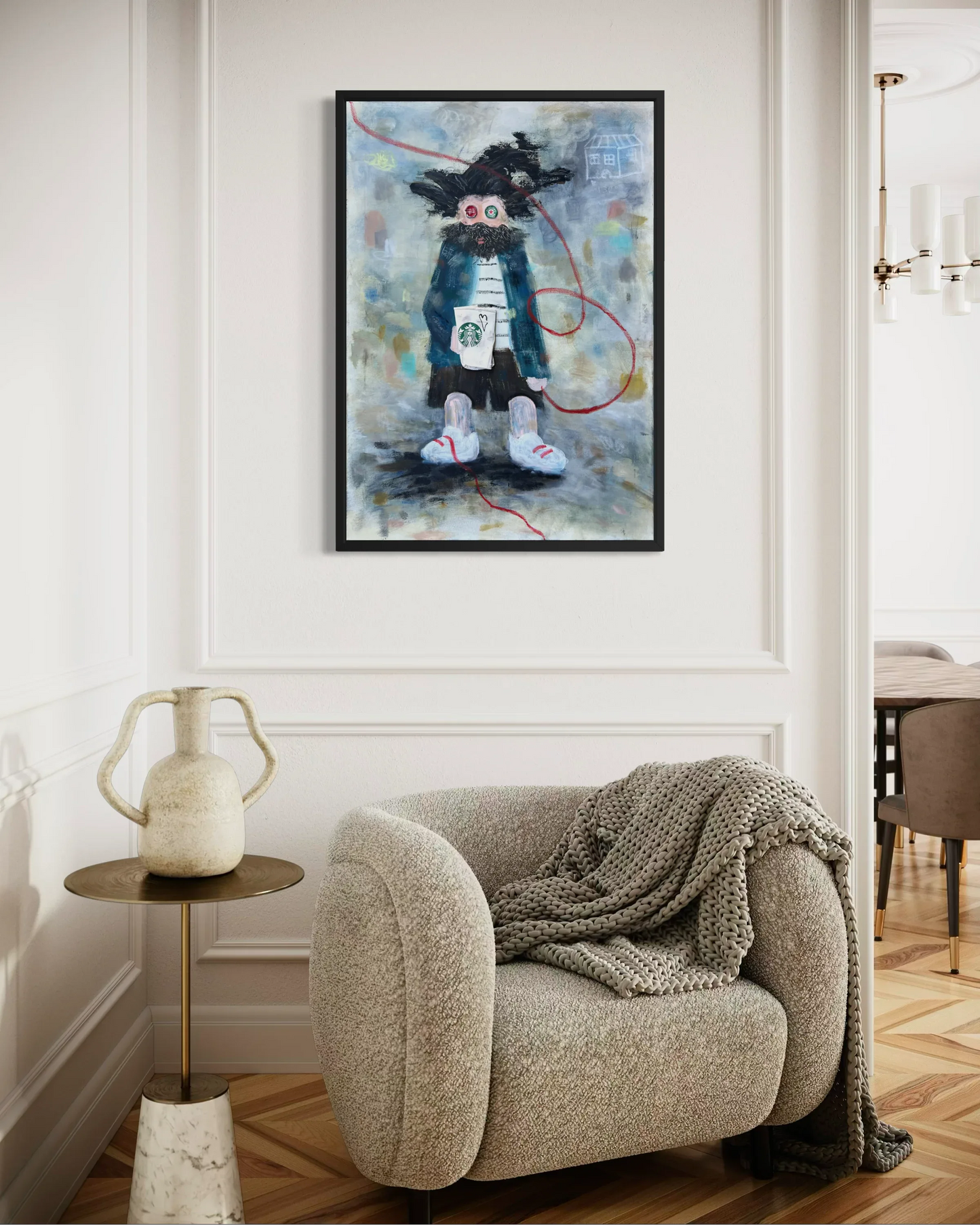 Framed abstract painting above a beige armchair with a textured blanket in a room setting.