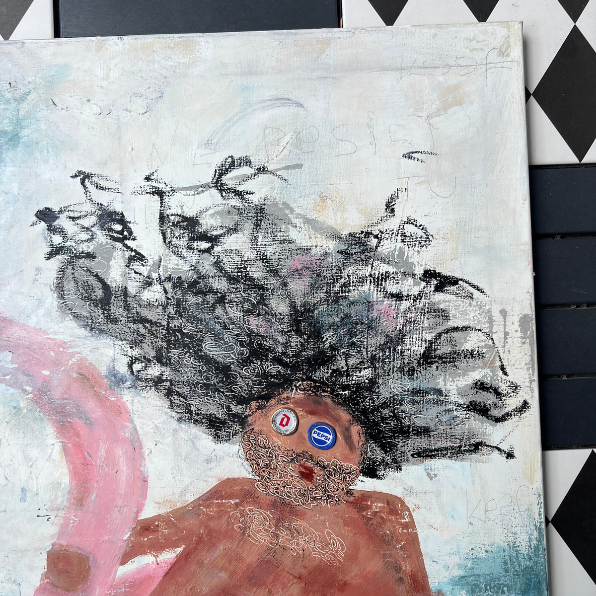 A square canvas painting featuring an expressive childlike figure with large black hair, a brown body, blue and white striped shorts, and pink flowing shapes, photographed against a black-and-white diamond-patterned surface.