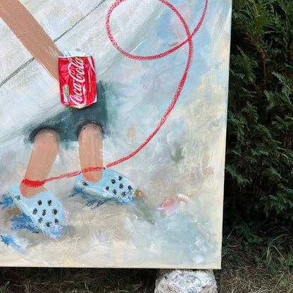 A close-up of a painted canvas showing a stylized figure holding a red Coca-Cola can, with blue-and-white dice and a red looped line, photographed outdoors on grass with a rock underneath the canvas.