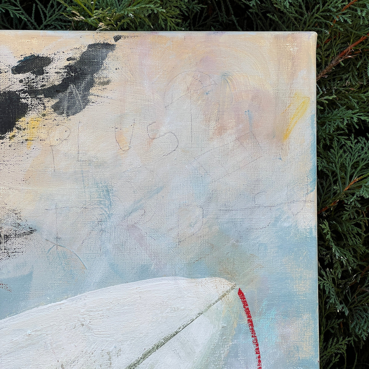 An abstract canvas painting with textured brushstrokes of white, light blue, beige, black, and a small red accent, photographed outdoors against green foliage.