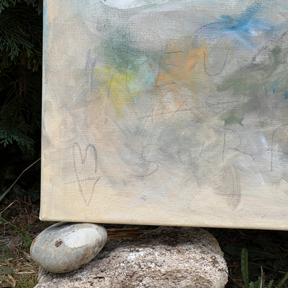 An abstract canvas painting resting outdoors on two large rocks, with green foliage and grass visible in the background.