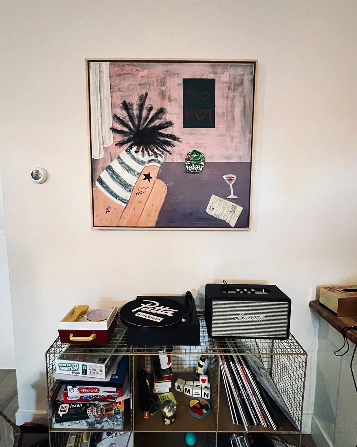 Room interior with a shelf displaying various items and a framed picture on the wall.